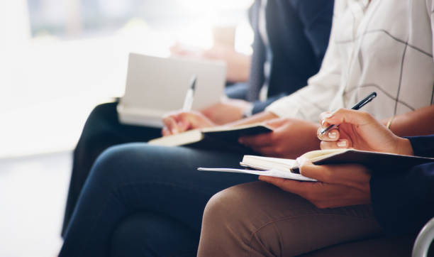 Cropped shot of unrecognizable businesspeople sitting and writing notes in a book while in the office during the day